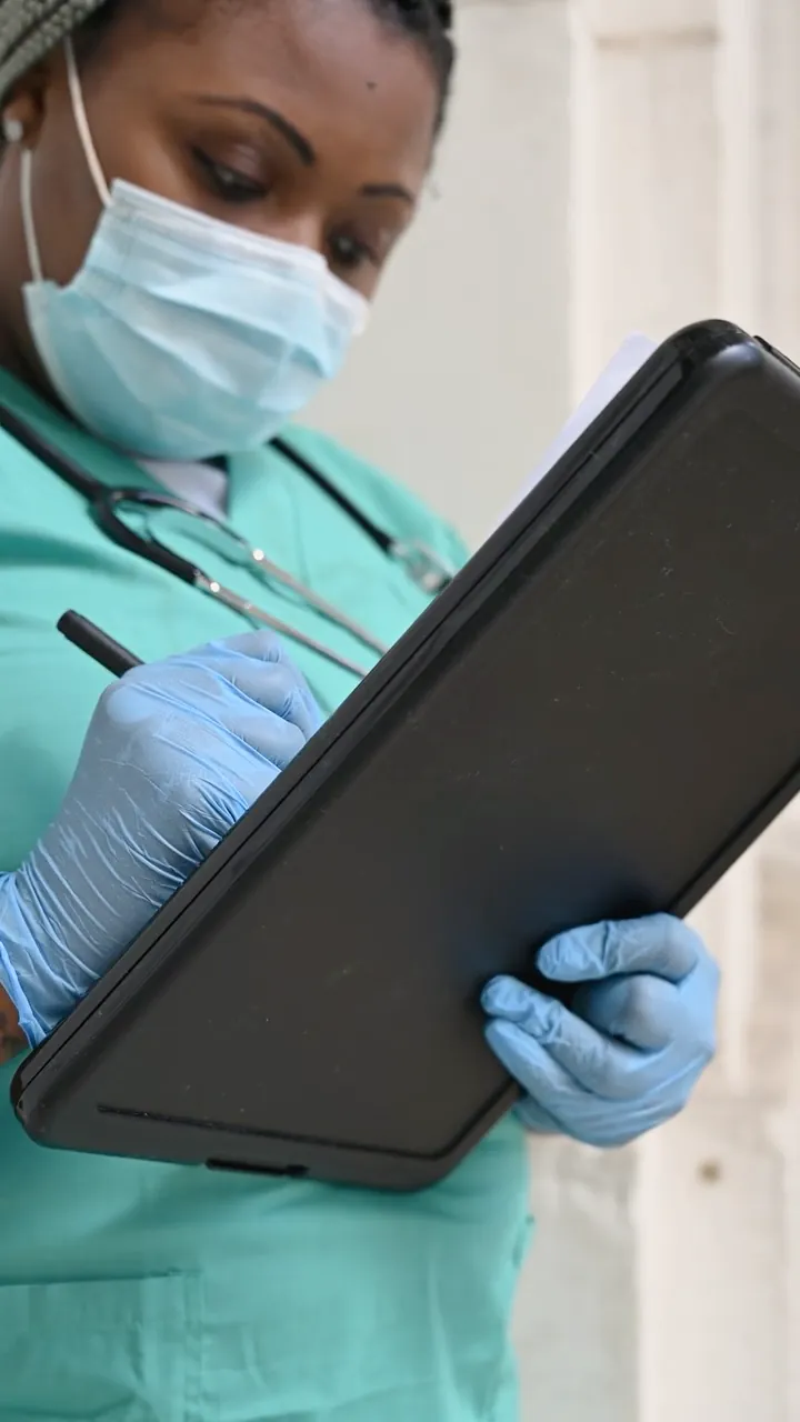 A nurse in teal scrubs writing on a clipboard